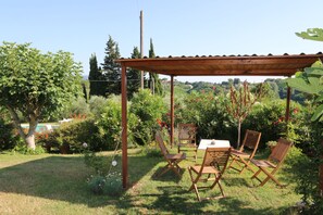 Un patio jardín con una mesa y sillas, rodeado de abundante vegetación y vistas al campo.