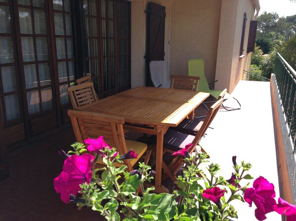 A wooden table and chairs on a balcony with a view of greenery.