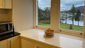 A kitchen with a microwave, a bowl on the counter, and a view of a lake and trees through large windows. - 3 bedroom 2nd floor apartment to sleeping 8 with stunning views of Loch Ness. (Loch Ness)