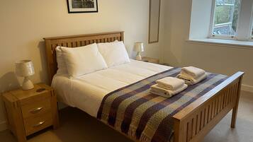 A neatly made bed with white linens, a wooden headboard, and a colorful woven blanket. There are two bedside tables with lamps and a framed picture on the wall.