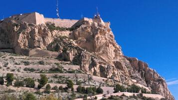 Una colina rocosa con una estructura fortificada en la cima, que cuenta con una escalera que conduce hasta ella.