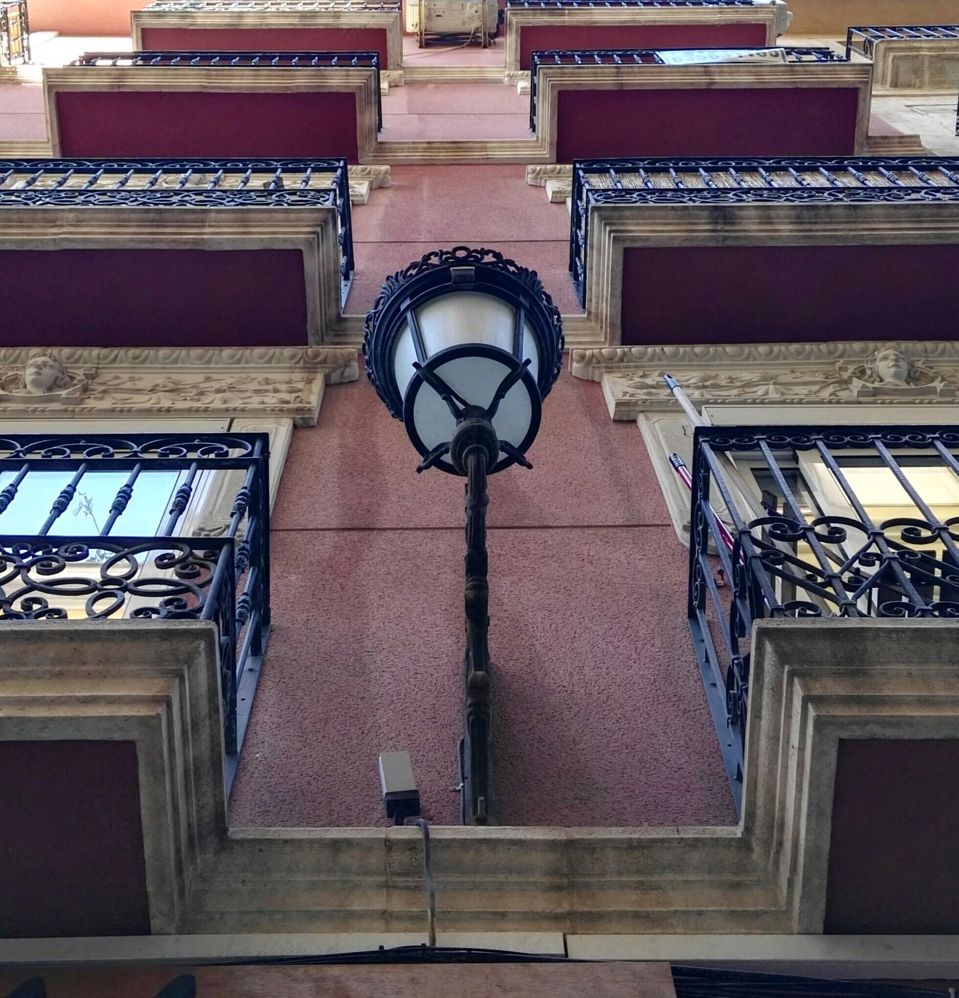 Vista del interior de un edificio, con una escalera central que sube a un balcón.
