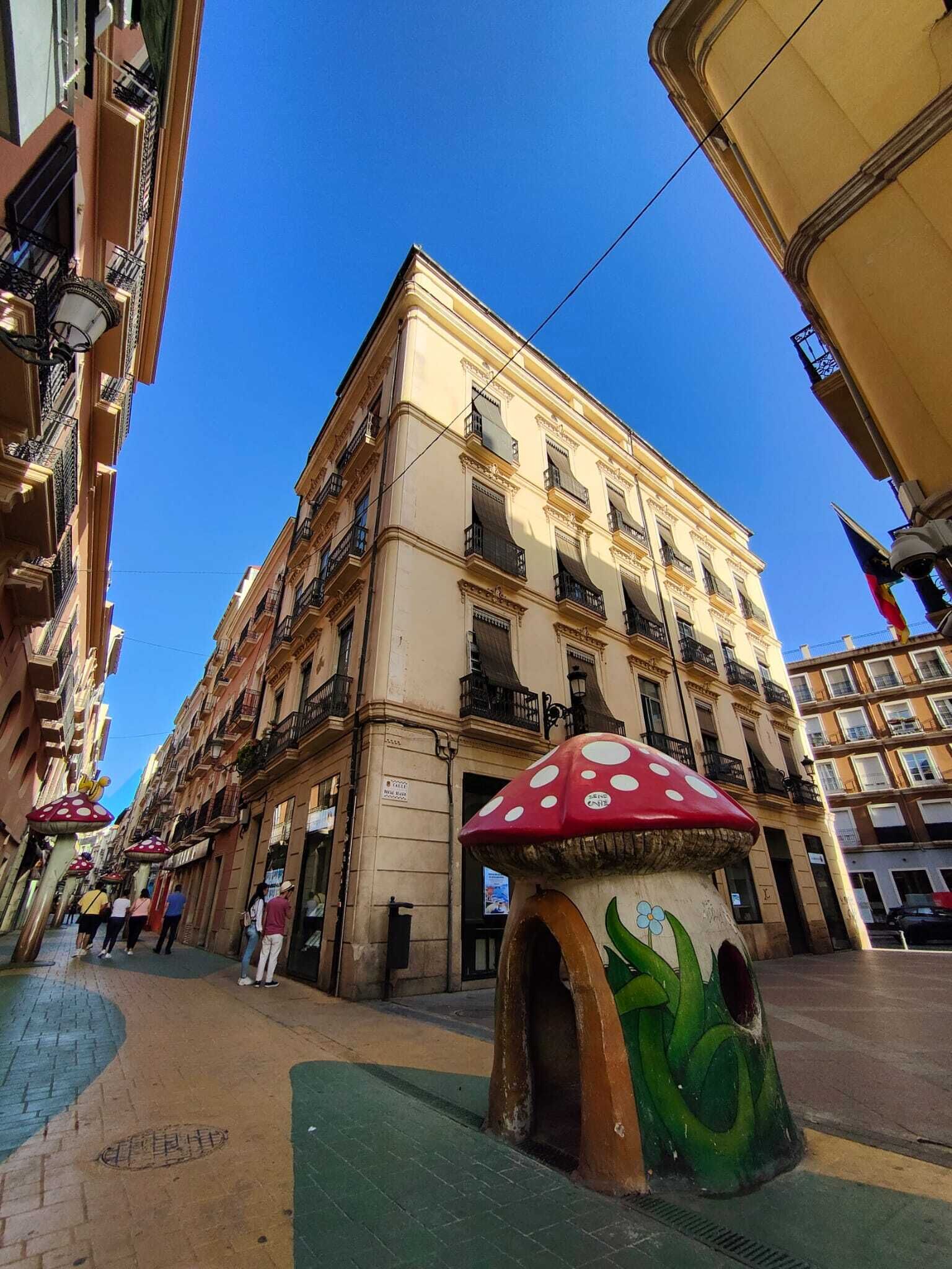 Un edificio con varios pisos, balcones y una gran escultura de hongo al frente.