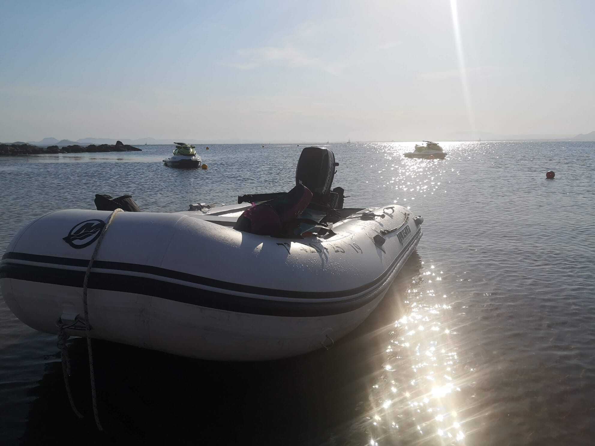 Una pequeña embarcación inflable atracada en aguas tranquilas, con cielo despejado y tierra a lo lejos.