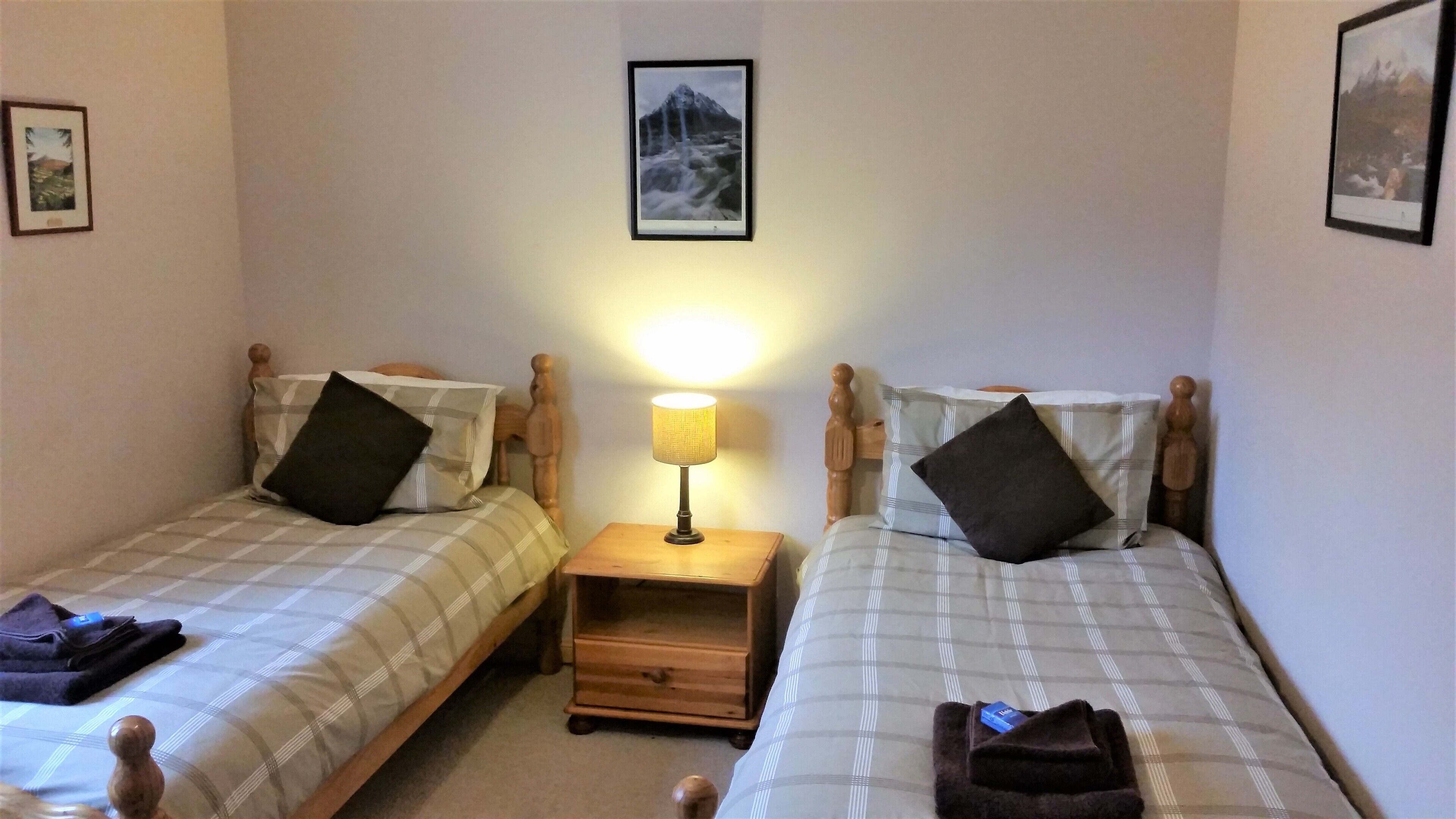 A twin room with two beds, a nightstand with a lamp, and a small wooden drawer.