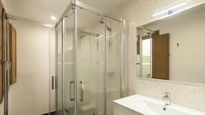 Ein modernes Badezimmer mit einer gläsernen Dusche, einem weißen Waschbecken und einem Spiegel darüber.