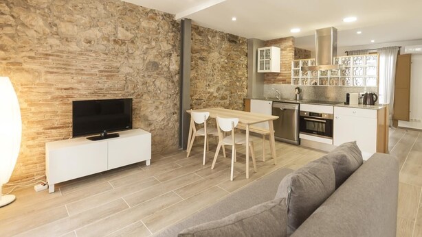 Ein modernes Wohnzimmer mit Steinwand, Flachbildfernseher, weißer Unterhaltungseinheit, grauem Sofa und Essbereich mit Tisch und Stühlen.