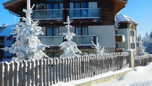 Eine Holzhütte mit Balkon, umgeben von schneebedeckten Bäumen und einem Holzzaun.