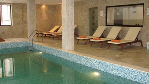 Ein Hallenbad mit klarem, blauem Wasser, umgeben von Liegestühlen mit orangefarbenen Handtüchern.