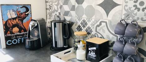 Un coin cuisine équipé d’une machine à café, d’une bouilloire, d’un porte-tasses et d’un plateau contenant un bocal et une boîte.