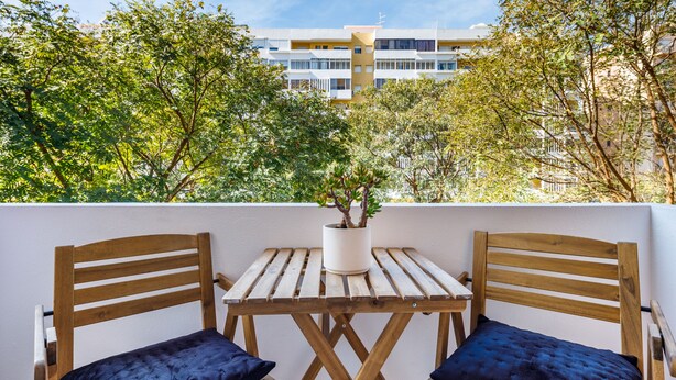 A wooden table with two chairs, a potted plant, and a view of a building in the background. - Kwadalayo Art Quarters (Faro)