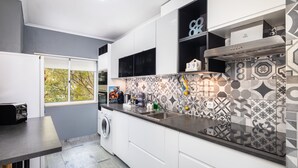 A modern kitchen with a large window, a washing machine, and patterned tiles. - Kwadalayo Art Quarters (Faro)