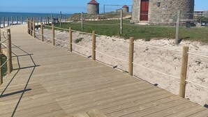 Ein hölzerner Steg führt zu Gebäuden mit roten Türen mit Blick auf einen Strand.