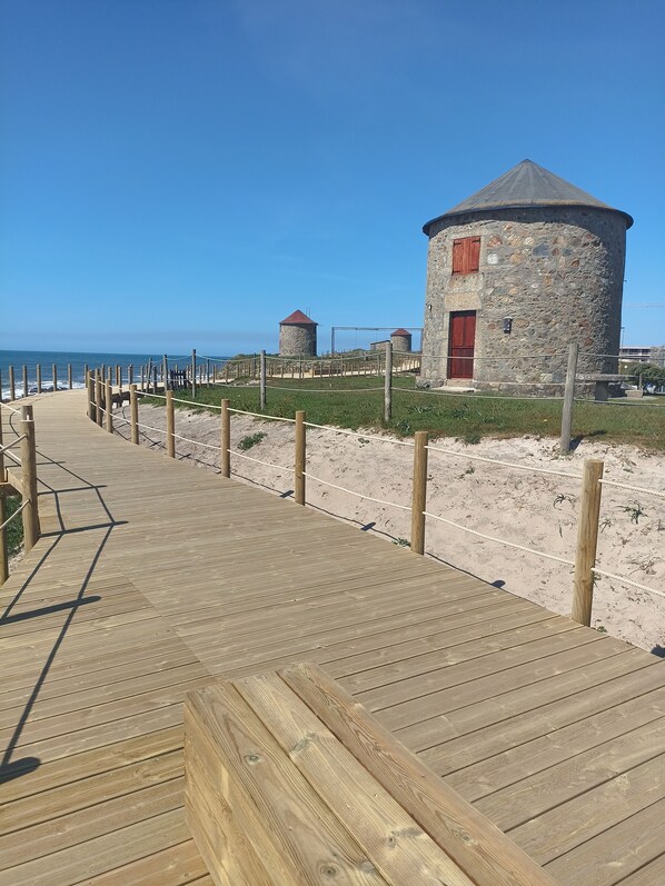 A wooden boardwalk leading to stone structures with red doors, overlooking a beach.