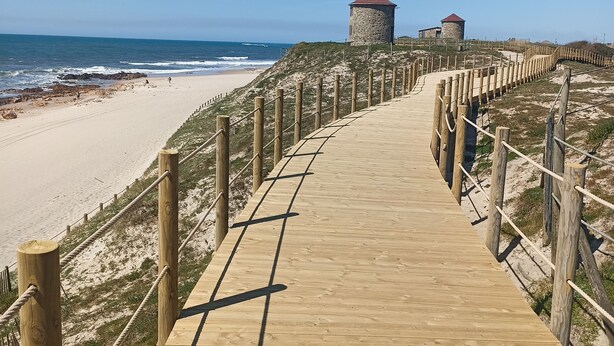 Ein hölzerner Steg führt zu Strandhütten mit freiem Blick auf den Ozean.