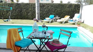 Ein Poolbereich mit einem Tisch für zwei Personen, einem Stuhl mit einem gelben Handtuch und einem weiteren mit einem rosa Hut.