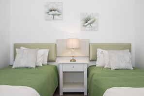 Een tweeepersoonskamer met twee bedden, een nachtkastje met een lamp, en twee bloemschilderijen aan de muur.