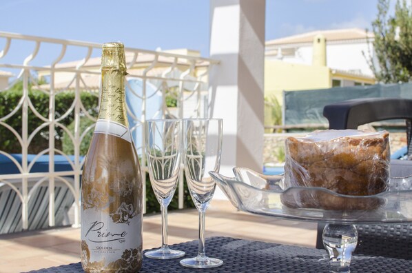 A bottle of champagne, two glasses, and a cake on a table outdoors.