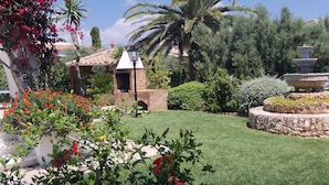 A garden with a brick structure, palm trees, and a fountain.
