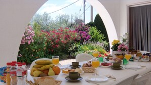 A breakfast table set outdoors with fruits, bread, and beverages.