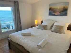 A neatly made bed with pillows and a rolled towel, a bedside lamp, and a painting of a beach scene.