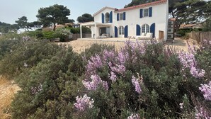 Una casa de dos pisos con un porche cubierto y un jardín con flores moradas.