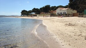 A beach with clear water, sandy shore, and buildings in the background. - Waterfront property renovated in 2024 (Hyères)