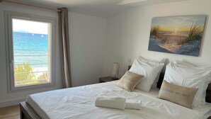 Un dormitorio con una cama grande, un cuadro de una escena de playa y una ventana con vista al mar.