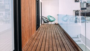 A wooden deck with a glass balustrade, two green chairs, and a view of buildings in the background. - Beautiful Villa for 6 people, WiFi, private and heated pool, 8min from the beach (Costa Adeje)