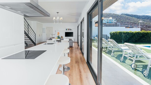 A modern kitchen with a long countertop, bar stools, and a view of a pool and mountains. - Beautiful Villa for 6 people, WiFi, private and heated pool, 8min from the beach (Costa Adeje)