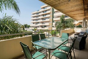 A balcony with a glass table and chairs, overlooking a building with multiple balconies and greenery. - VilamouraSun Aquamar 110 -  Pool and Marina View (Quarteira)