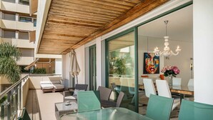 Een buitenruimte met eettafels en stoelen van glas, een houten plafond en uitzicht op het interieur van het gebouw.