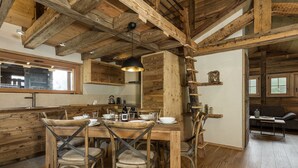 Un intérieur rustique en bois, avec un coin repas comprenant une table et des chaises en bois, un luminaire suspendu et des poutres apparentes au plafond.