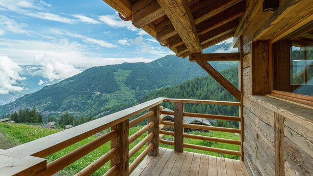 Un balcon en bois, doté d’une balustrade en bois, qui offre une vue sur un paysage montagneux.