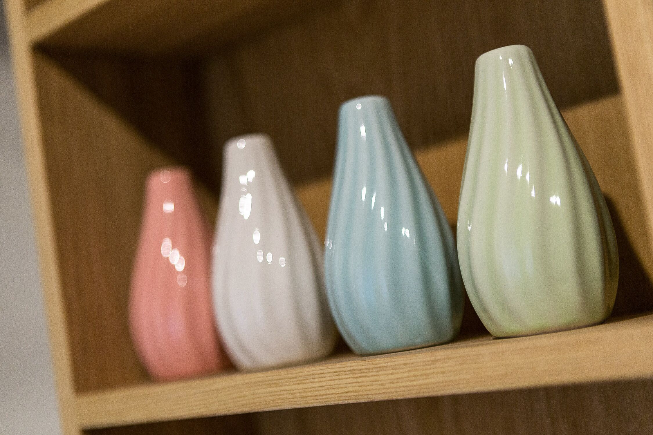 Four ceramic vases on a wooden shelf.