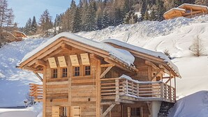 Une cabane en bois dotée d’un balcon, entourée d’arbres couverts de neige et surplombant un ciel dégagé.