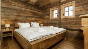Une chambre de style cabane en bois, avec un lit en bois, deux tables de chevet et deux fenêtres.