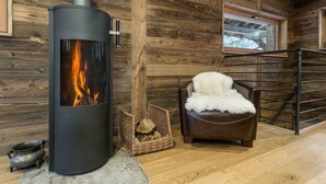 L’intérieur d’un chalet moderne en bois, doté d’un poêle à bois, d’un fauteuil en cuir et d’une fenêtre donnant sur le paysage enneigé.