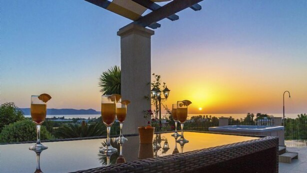 Una terraza con piscina, con vistas a una puesta de sol y cuatro vasos de una bebida.