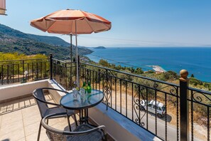 Un balcon avec une table, des chaises et un parasol, offrant une vue sur la côte, avec une route et une voiture garée.