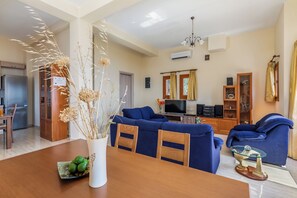 A living room with a blue sofa, wooden dining table, and a vase with dried plants.