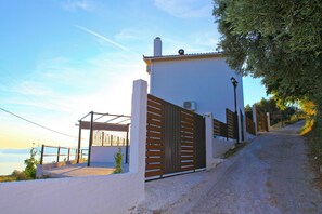 A gated entrance with a white building, a wooden fence, and a paved path leading to a covered area with a view of the sea. - Villa DISI with private pool at the  best prices. (Skopelos)