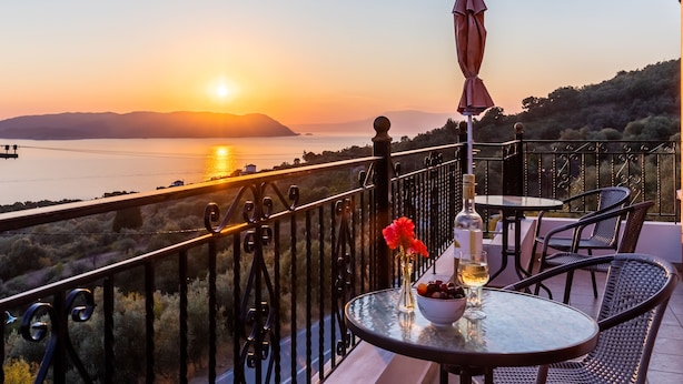 Un balcon avec une table, des chaises et une vue sur le coucher de soleil sur l’eau.