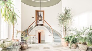 Un hall d’entrée spacieux, agrémenté d’un magnifique escalier, de nombreuses plantes en pot et d’une urne décorative.