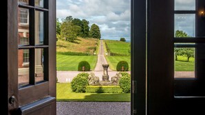 Une vue à travers une porte ouverte, donnant sur un jardin bien entretenu, avec un chemin menant à un bâtiment.