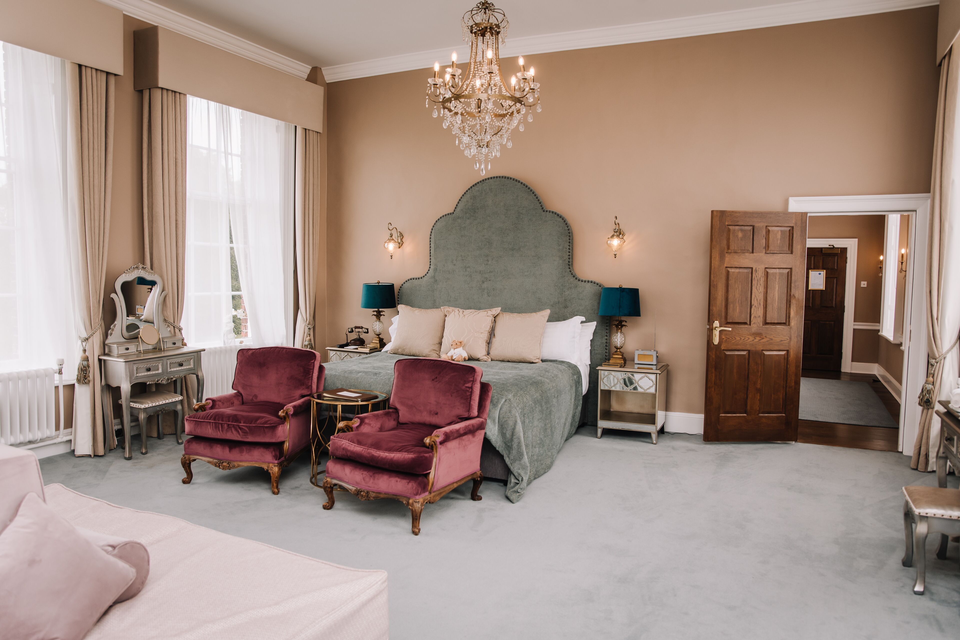 A bedroom with a large bed, two armchairs, a dresser, and a chandelier.