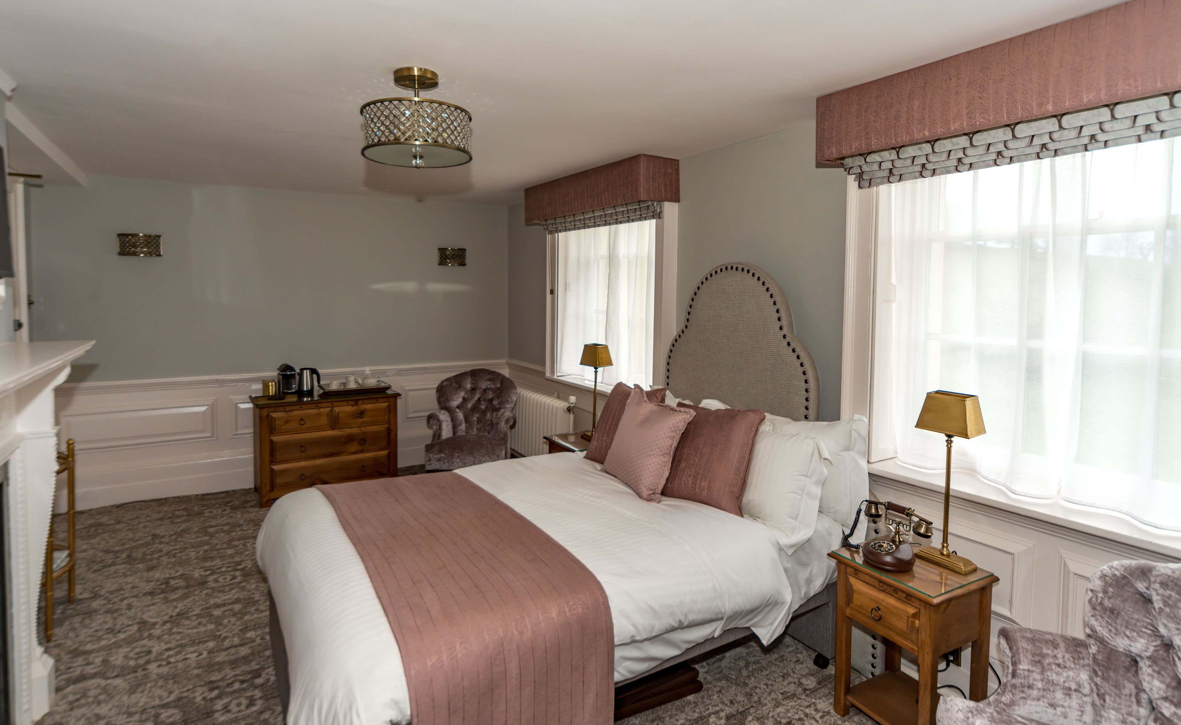 A bedroom with a large bed, a dresser, a chair, a lamp, and a window with curtains.