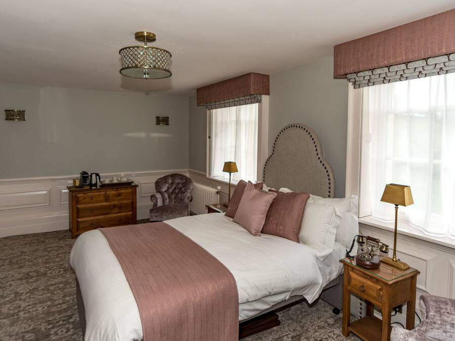 A bedroom with a large bed, a dresser, a chair, a lamp, and a window with curtains.