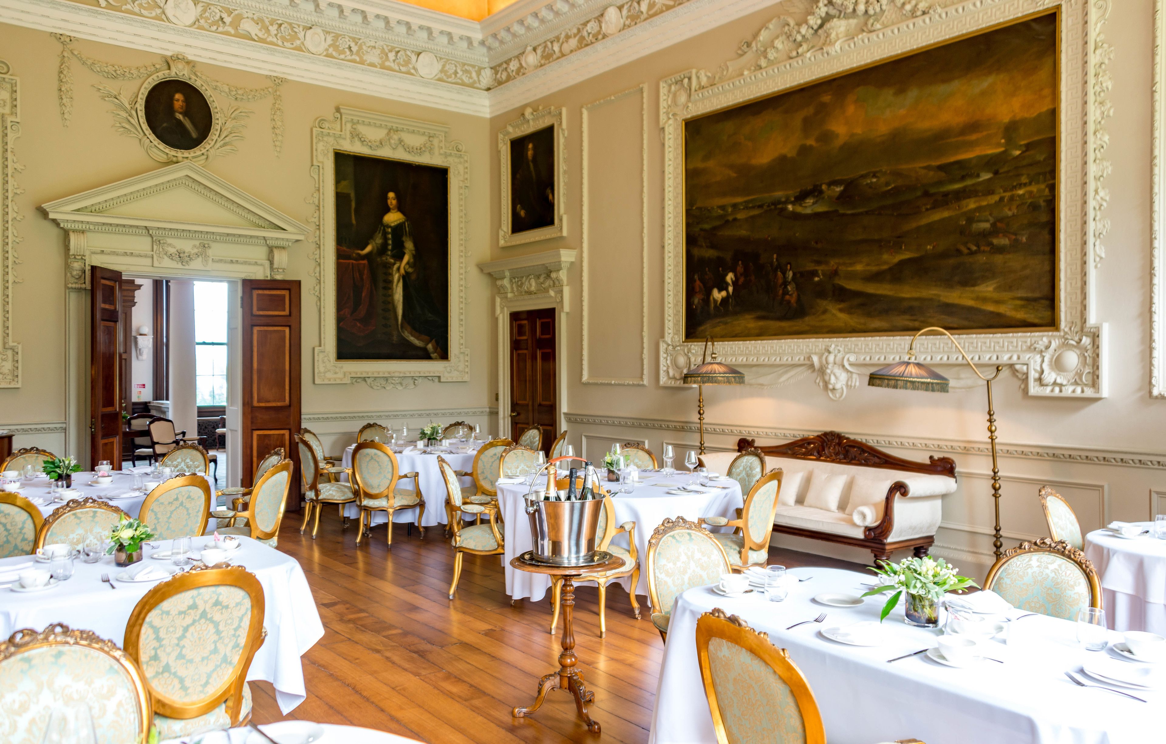 A formal dining room with ornate decor, multiple tables set for dining, and classical paintings on the walls.