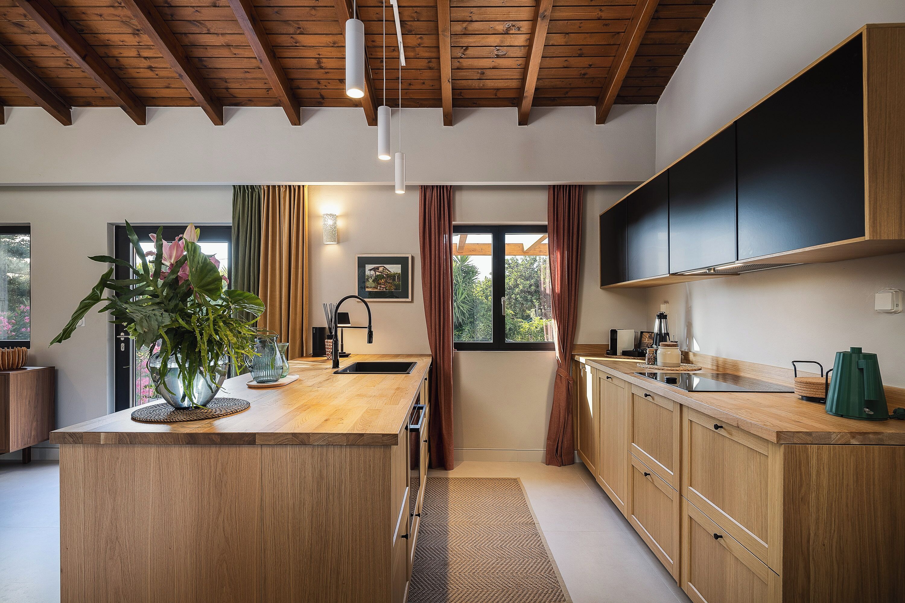 A modern kitchen with wooden cabinets, a central island, and a view to the outside.